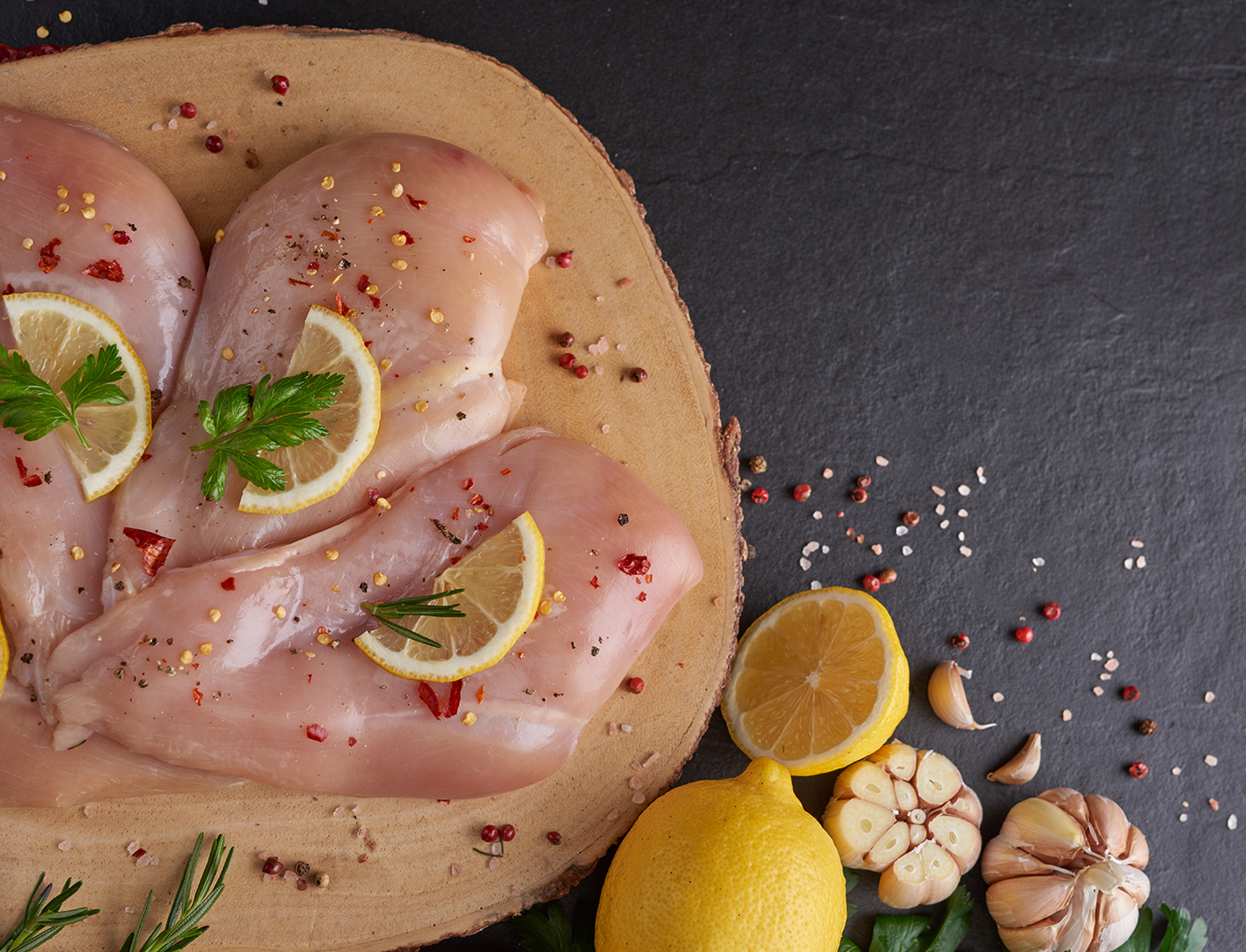 raw chicken fillet with garlic, pepper and rosemary on wooden on